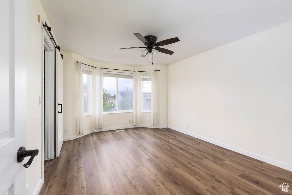 Spare room with a ceiling fan, baseboards, a barn door, and wood finished floors