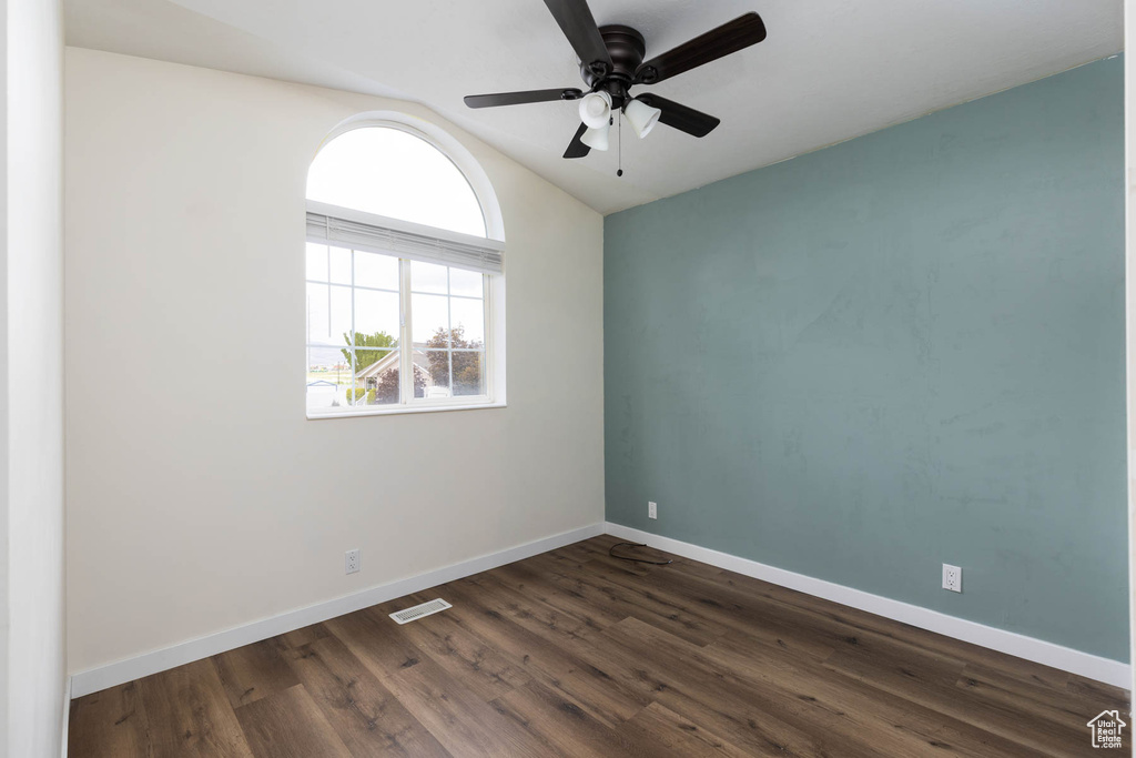 Spare room with visible vents, dark wood-style flooring, lofted ceiling, baseboards, and a ceiling fan