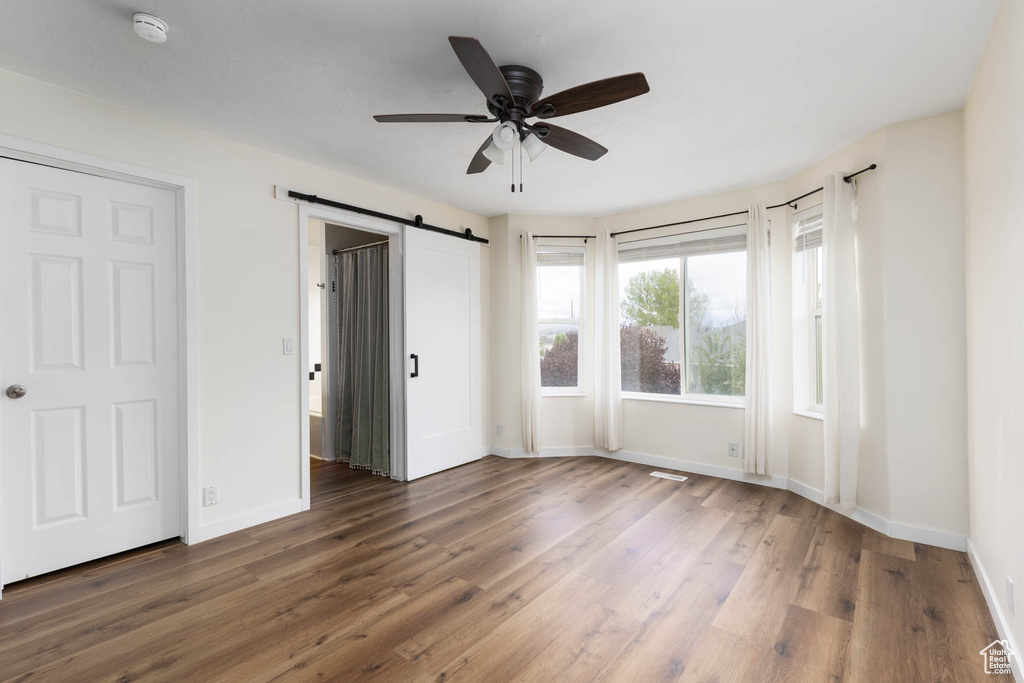 Unfurnished bedroom with a ceiling fan, visible vents, a barn door, wood finished floors, and baseboards
