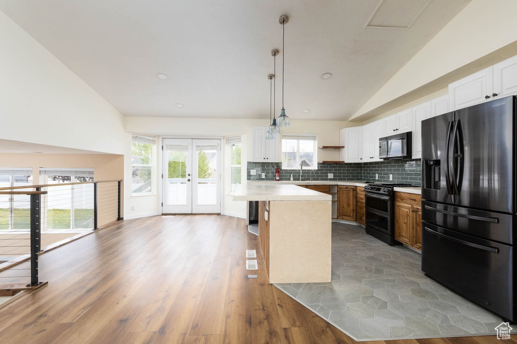 Kitchen featuring decorative backsplash, open shelves, vaulted ceiling, light countertops, and black appliances