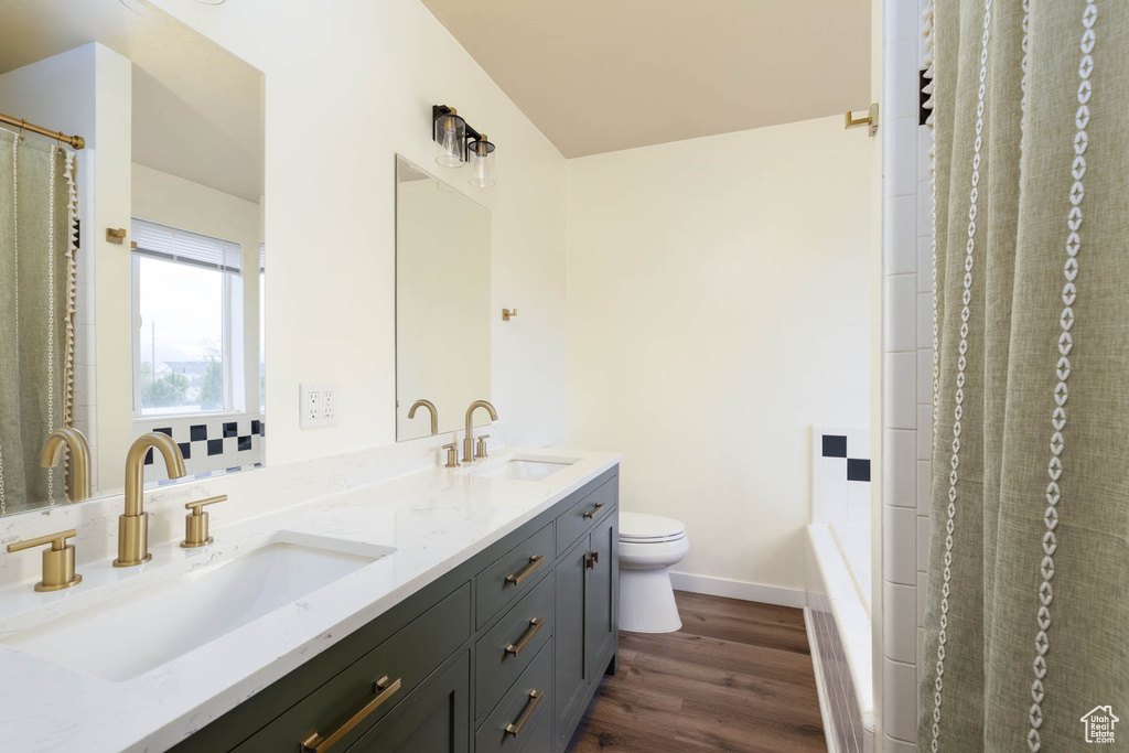 Bathroom with a sink, double vanity, toilet, and wood finished floors