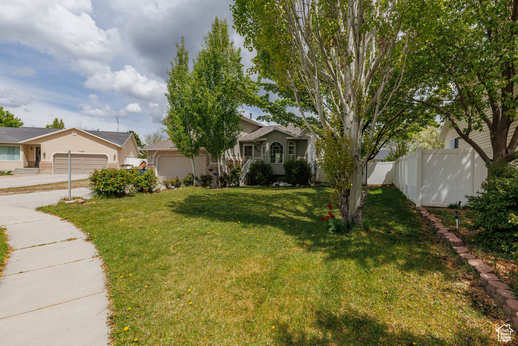 View of front facade featuring fence, an attached garage, concrete driveway, and a front yard