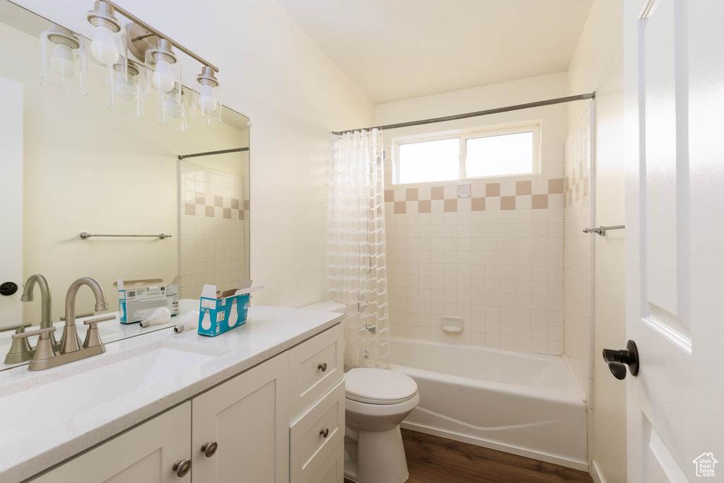Full bath featuring toilet, shower / bath combination with curtain, wood finished floors, and vanity