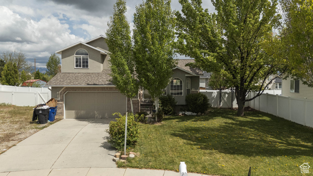 Obstructed view of property with fence, a shingled roof, an attached garage, a front lawn, and concrete driveway