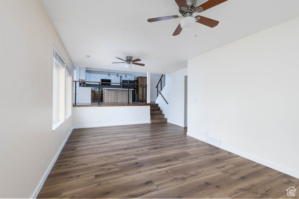 Unfurnished living room featuring stairs, ceiling fan, baseboards, and wood finished floors