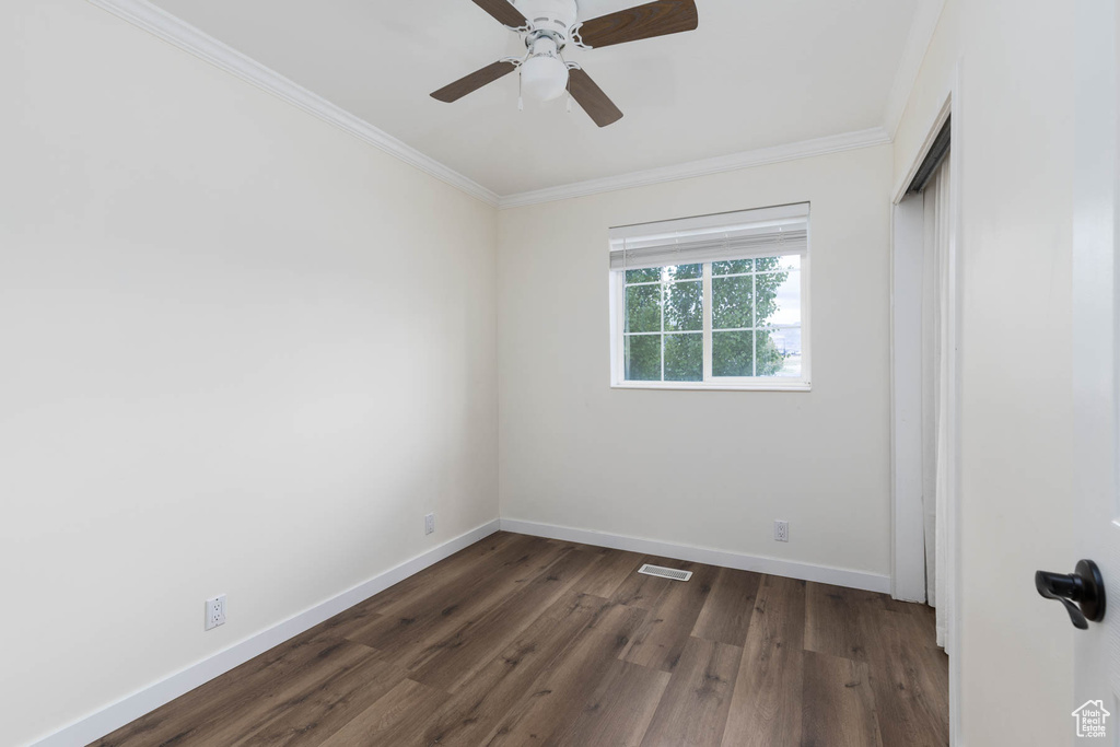 Empty room with crown molding, visible vents, baseboards, ceiling fan, and dark wood-type flooring