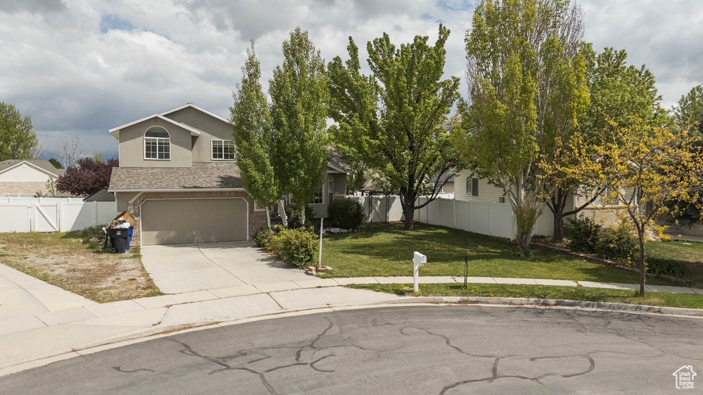 View of property hidden behind natural elements featuring a garage, a front lawn, fence, stucco siding, and concrete driveway