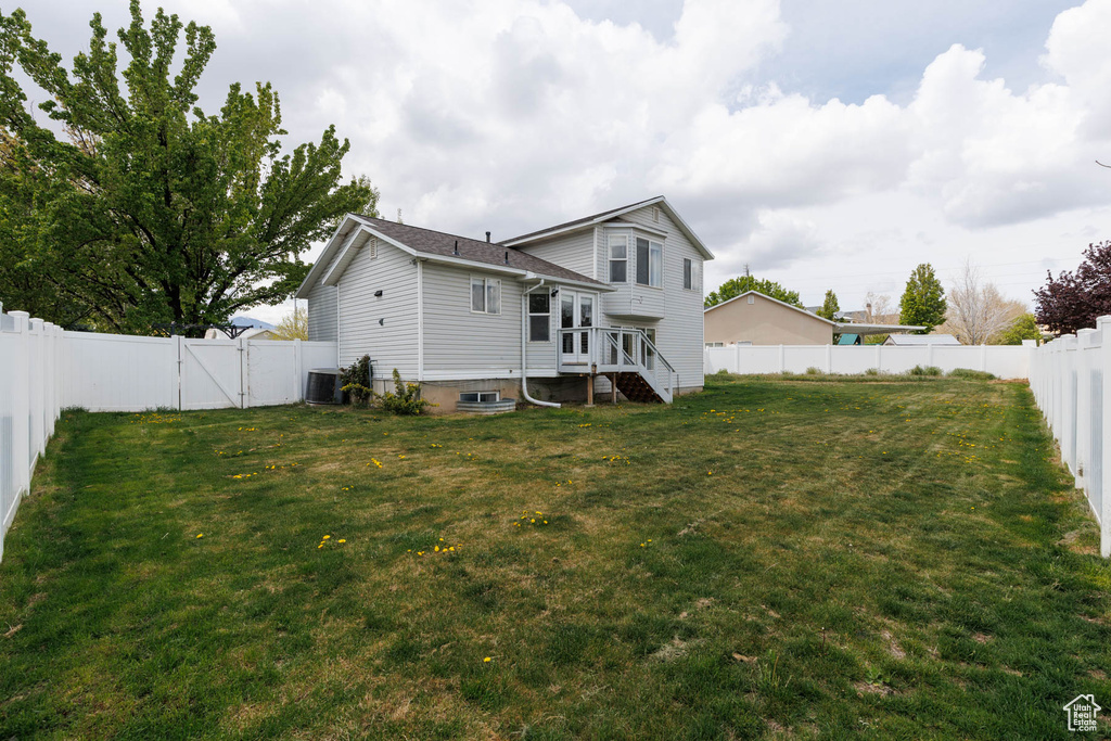 Back of property with a lawn, a fenced backyard, central AC, and a gate