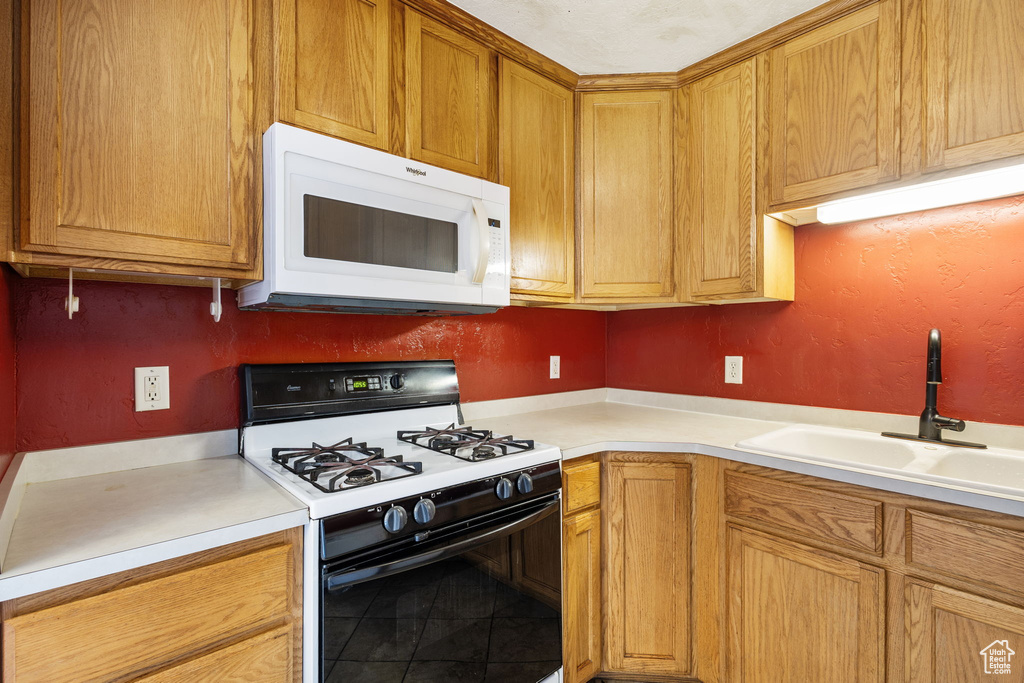 Kitchen featuring brown cabinetry, white microwave, gas range, light countertops, and a sink