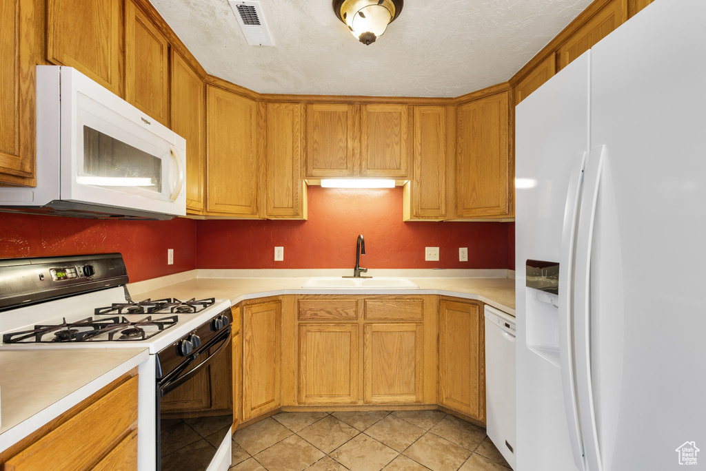 Kitchen with a sink, white appliances, light countertops, light tile patterned floors, and visible vents