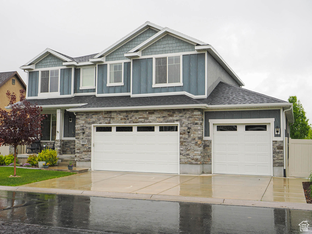 Craftsman inspired home featuring roof with shingles, an attached garage, stone siding, board and batten siding, and driveway
