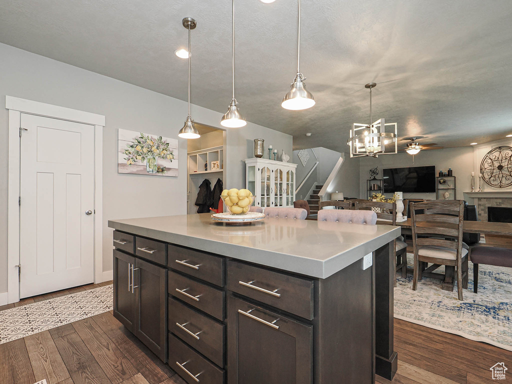 Kitchen with hanging light fixtures, dark brown cabinets, light countertops, dark wood-style floors, and open floor plan