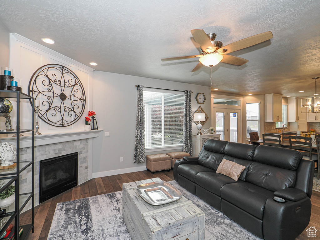 Living area featuring a textured ceiling, a glass covered fireplace, a wealth of natural light, and ceiling fan with notable chandelier
