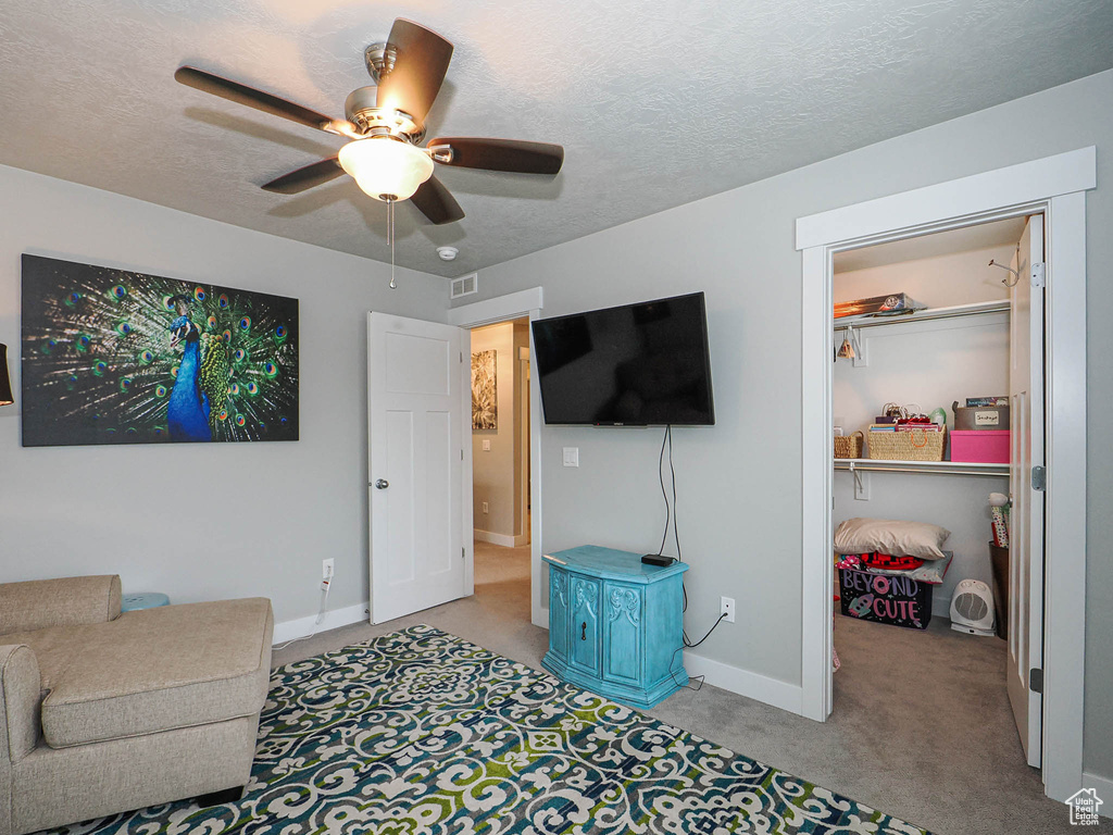 Living area featuring baseboards, ceiling fan, light carpet, and a textured ceiling