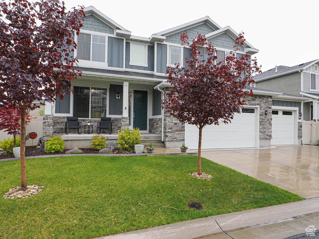 Craftsman-style house with a front yard, covered porch, stone siding, and concrete driveway
