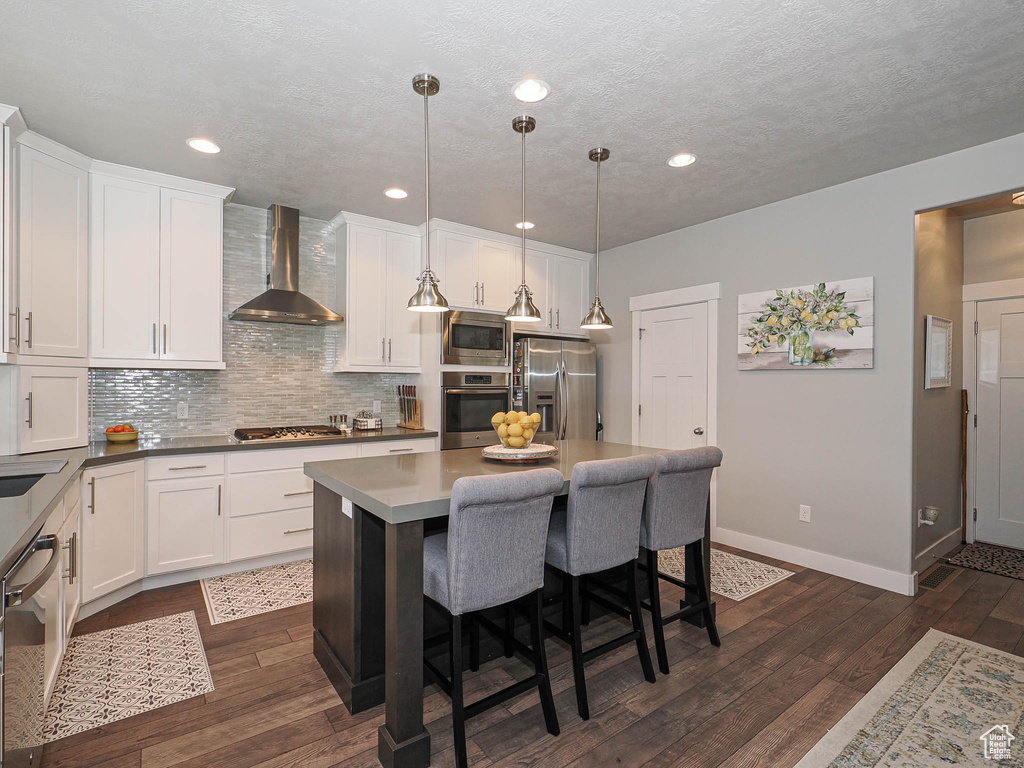 Kitchen with decorative backsplash, appliances with stainless steel finishes, baseboards, white cabinets, and wall chimney exhaust hood