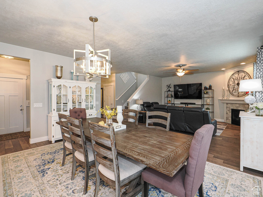 Dining space featuring stairs, wood finished floors, a fireplace, baseboards, and ceiling fan with notable chandelier