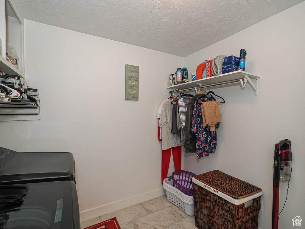 Clothes washing area featuring laundry area, a textured ceiling, baseboards, and washing machine and clothes dryer