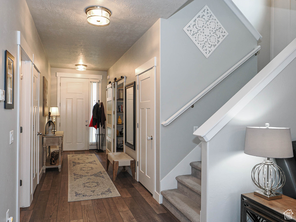 Foyer featuring stairway, a barn door, dark wood-style floors, and a textured ceiling