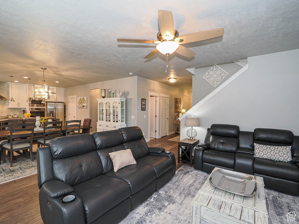 Living area featuring a textured ceiling, ceiling fan with notable chandelier, and dark wood-style floors