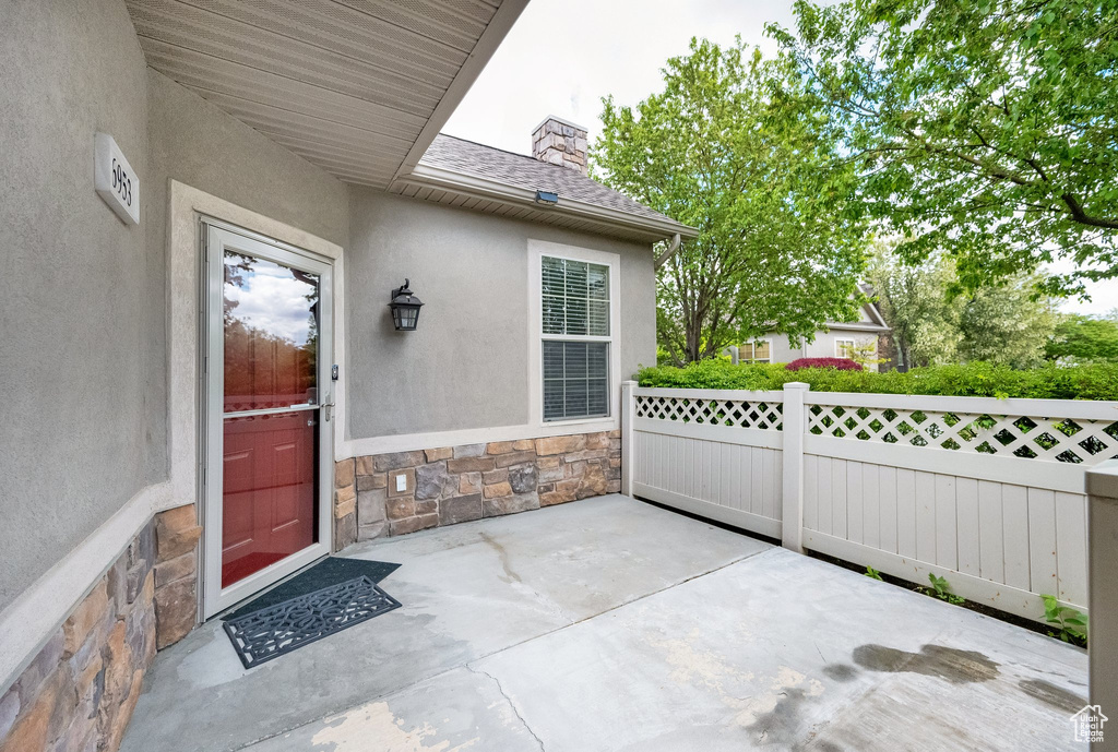 View of exterior entry featuring fence, a patio, stucco siding, and stone siding