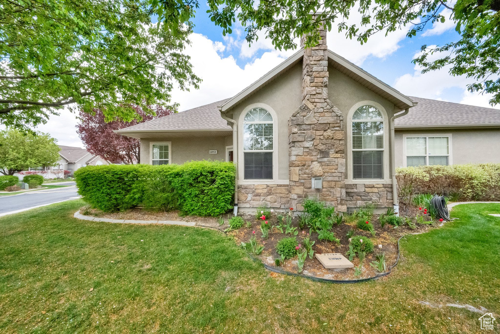 View of side of property featuring a lawn, stucco siding, stone siding, and a chimney
