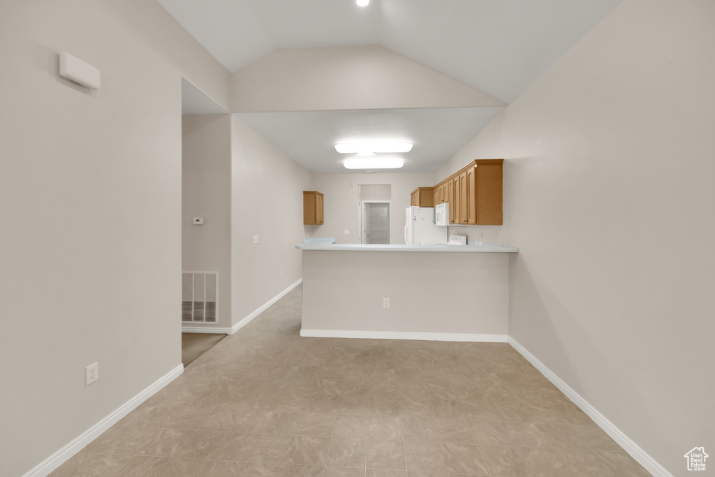 Kitchen with visible vents, freestanding refrigerator, a peninsula, light countertops, and brown cabinets