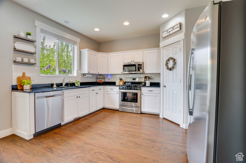 Kitchen with dark countertops, appliances with stainless steel finishes, a sink, and light wood-type flooring