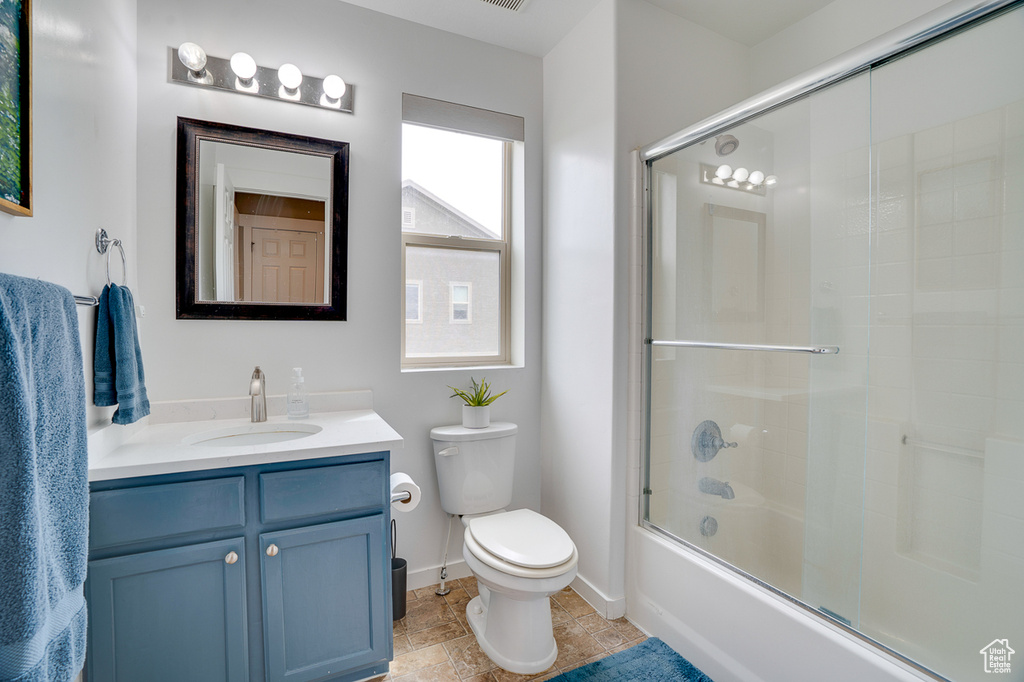 Bathroom with stone finish flooring, vanity, baseboards, bath / shower combo with glass door, and toilet