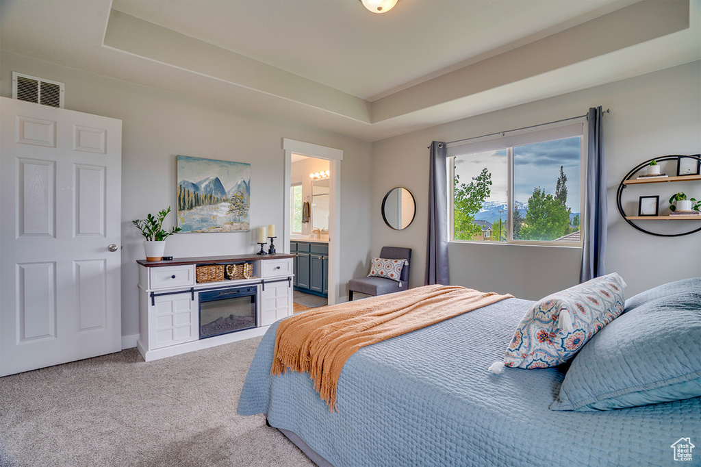 Bedroom featuring visible vents, a raised ceiling, ensuite bath, and light carpet