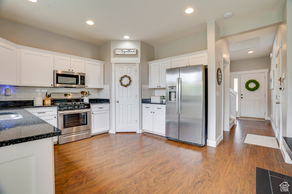 Kitchen featuring white cabinets, appliances with stainless steel finishes, wood finished floors, and tasteful backsplash