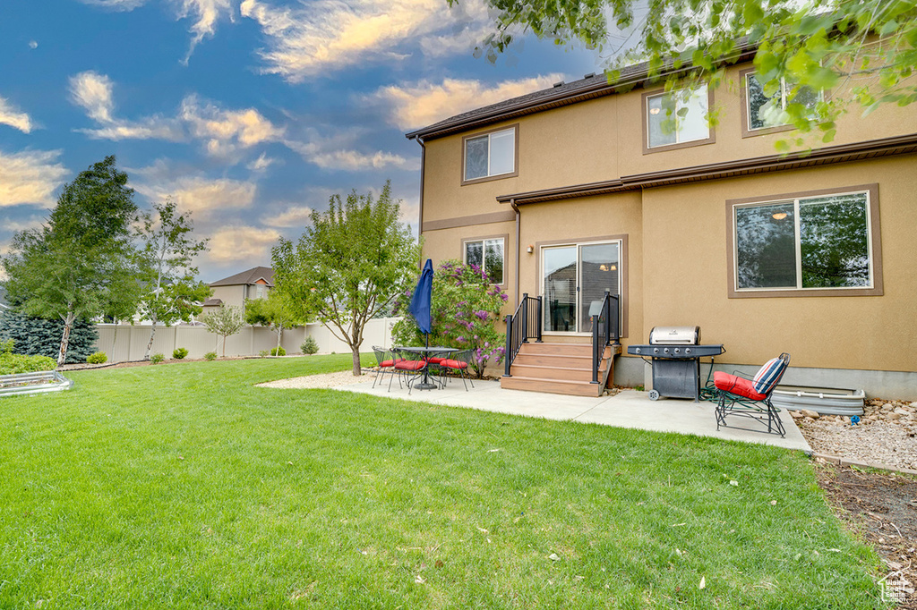 Back of property with fence, stucco siding, entry steps, a lawn, and a patio