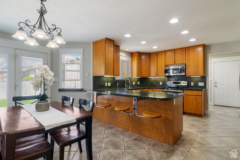 Kitchen with a peninsula, brown cabinets, tasteful backsplash, a sink, and stainless steel appliances