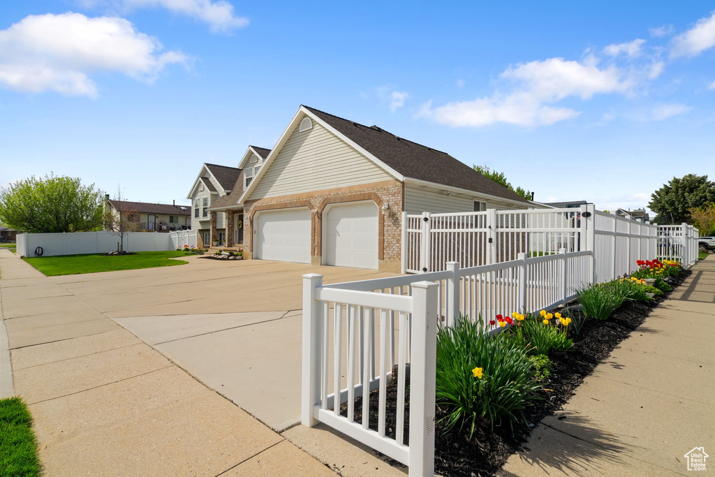 View of property exterior with brick siding, a garage, driveway, and fence private yard
