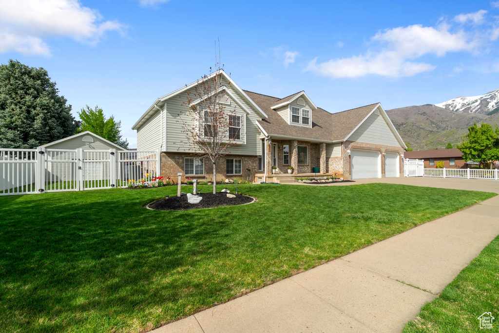 Split level home featuring fence, a gate, a front lawn, and brick siding