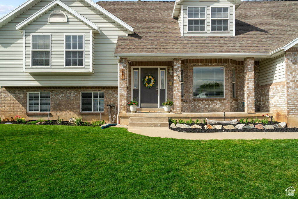 View of front facade with a shingled roof, a front lawn, and brick siding