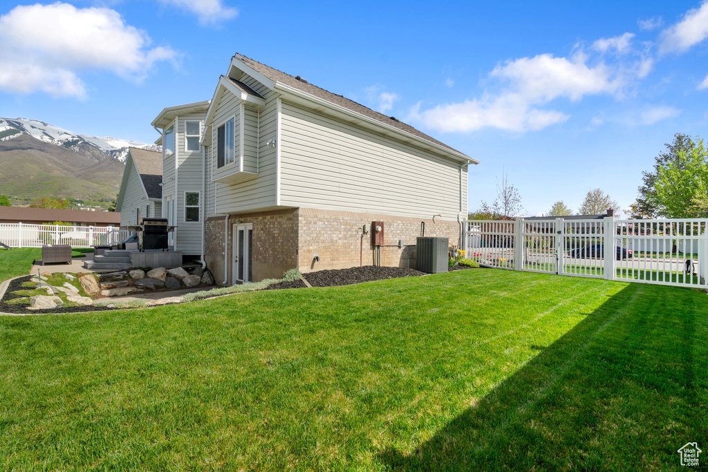 View of property exterior featuring brick siding, a lawn, fence, and a mountain view