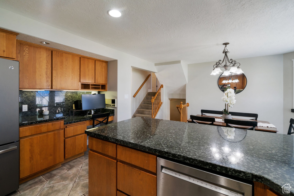 Kitchen featuring decorative backsplash, a textured ceiling, pendant lighting, appliances with stainless steel finishes, and brown cabinets