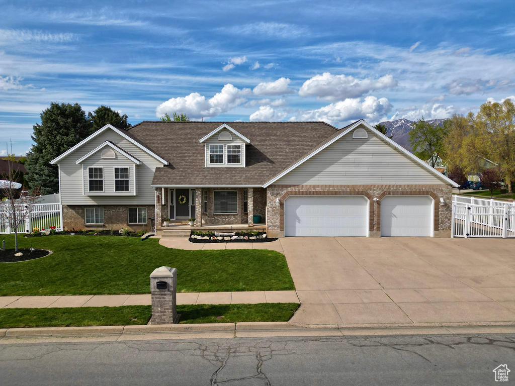 Tri-level home with fence, a front yard, brick siding, an attached garage, and driveway