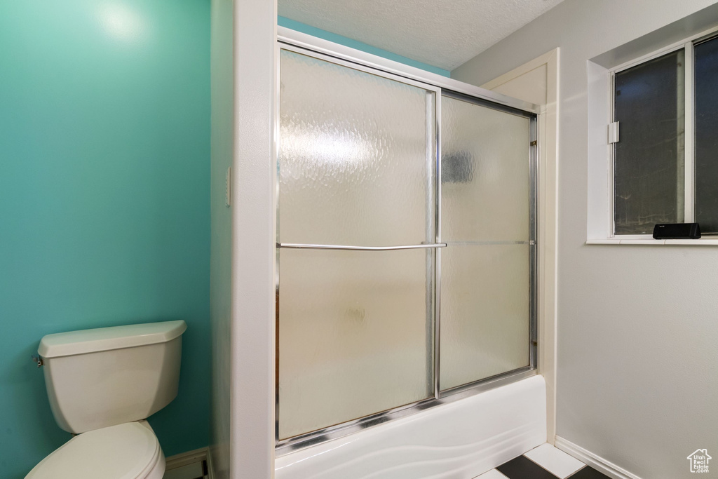 Full bath with toilet, baseboards, and shower / bath combination with glass door