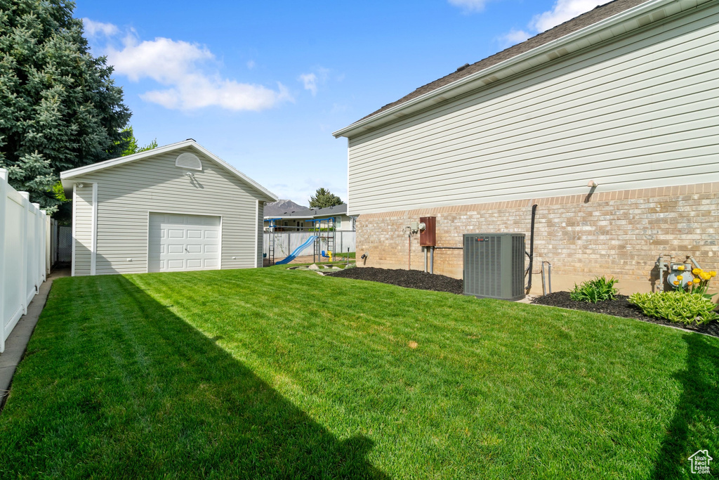 View of yard with central air condition unit, an outbuilding, a fenced backyard, and a garage
