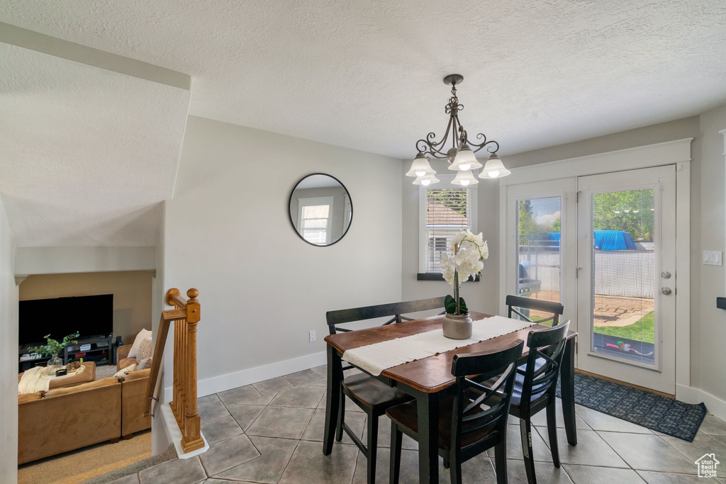 Tiled dining area featuring a textured ceiling, a notable chandelier, and baseboards