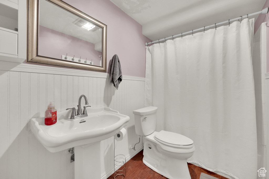 Full bath featuring a sink, toilet, a wainscoted wall, curtained shower, and wood finished floors