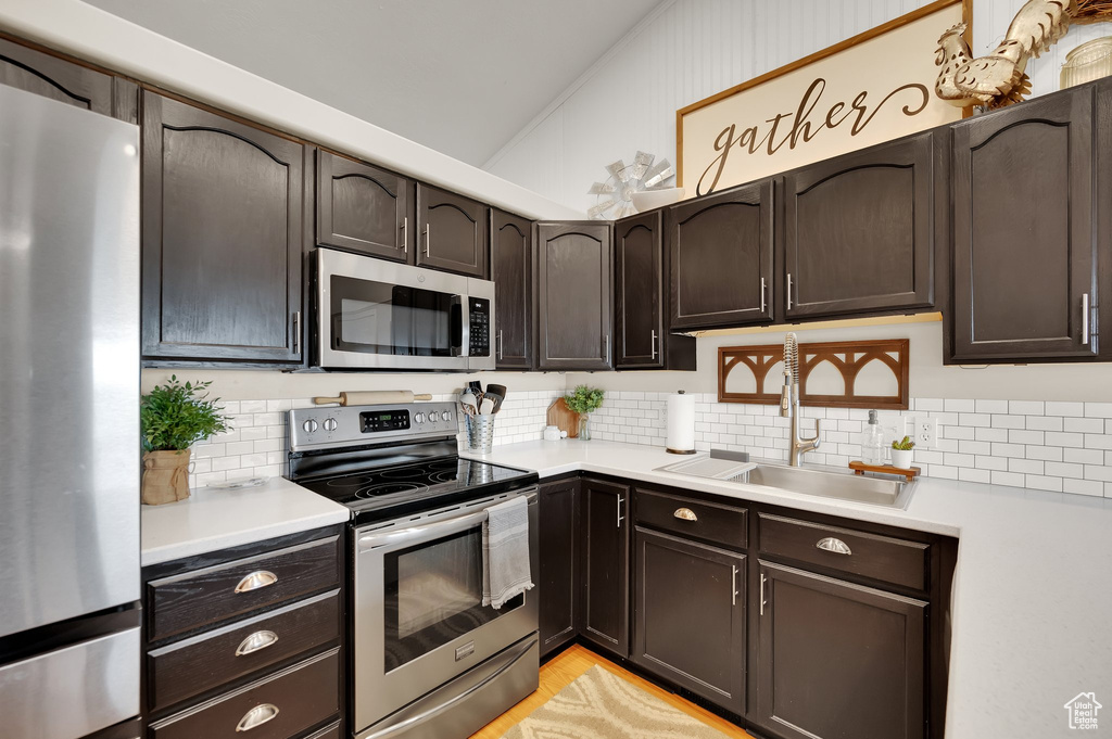 Kitchen with dark brown cabinetry, a sink, light countertops, stainless steel appliances, and backsplash