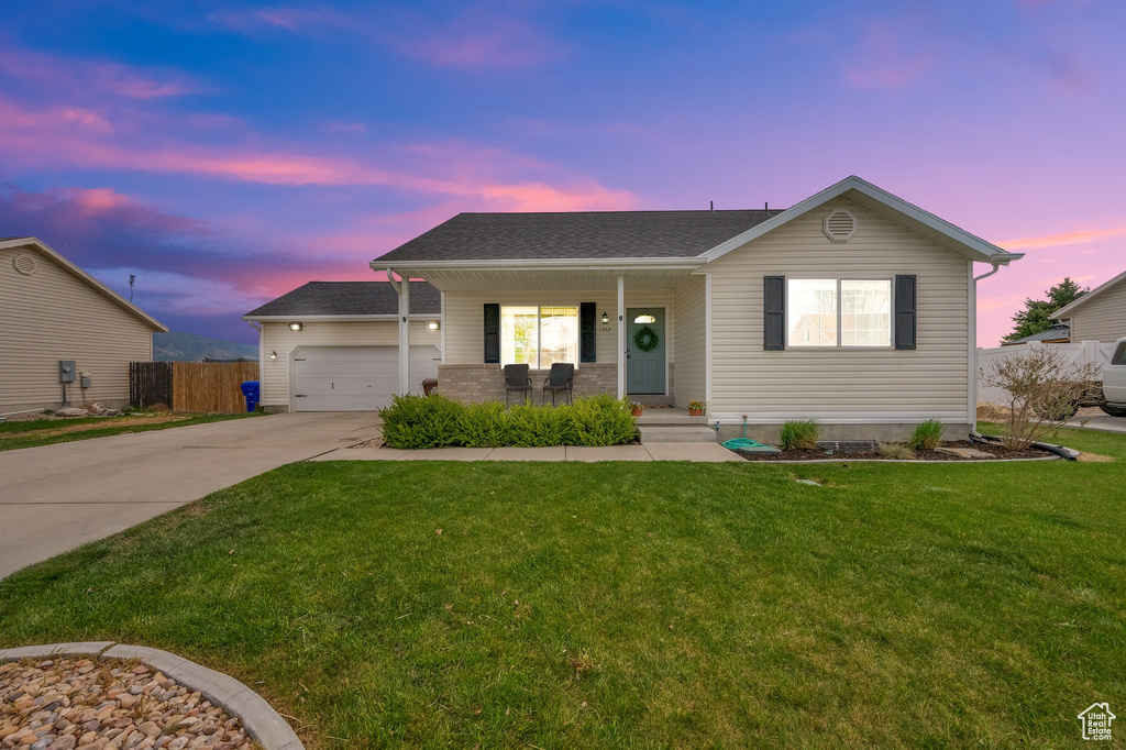 Ranch-style house featuring covered porch, a lawn, a garage, fence, and concrete driveway