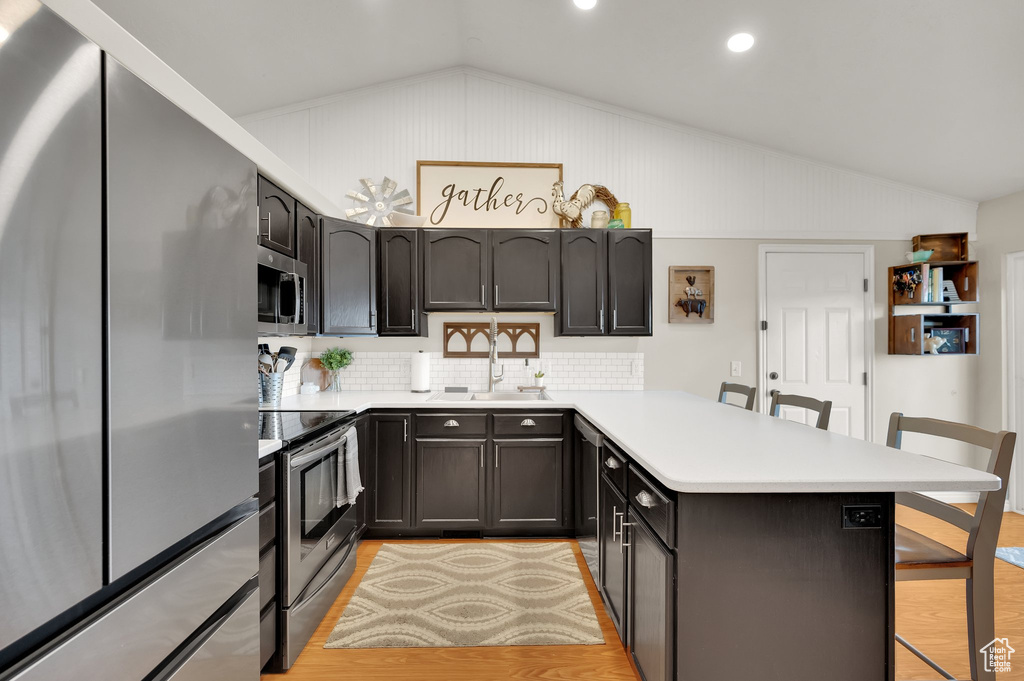 Kitchen featuring a peninsula, a kitchen bar, a sink, appliances with stainless steel finishes, and vaulted ceiling