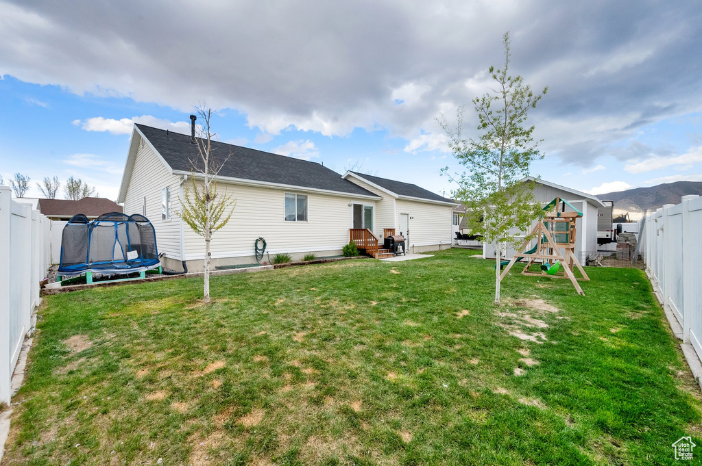 Back of house with a playground, a trampoline, a lawn, and a fenced backyard