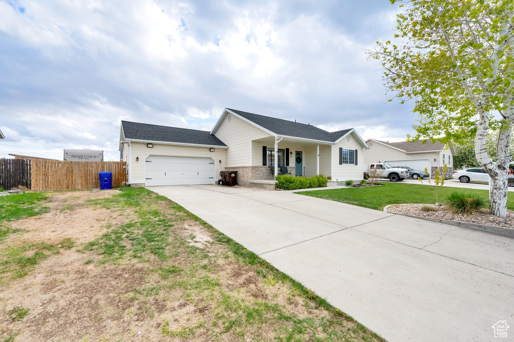 Single story home with a front lawn, fence, covered porch, an attached garage, and driveway