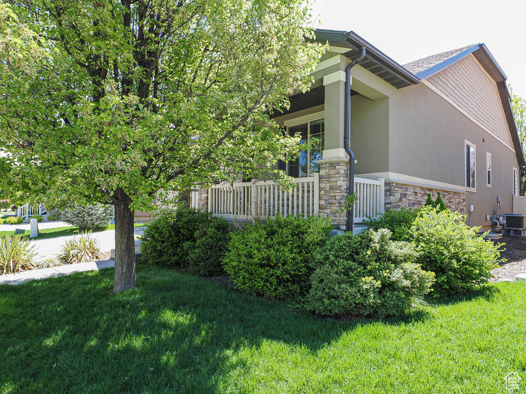 View of property exterior with stone siding, stucco siding, central AC unit, covered porch, and a yard