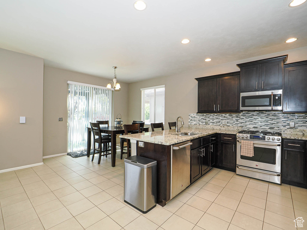Kitchen with decorative backsplash, appliances with stainless steel finishes, light stone countertops, a sink, and an inviting chandelier